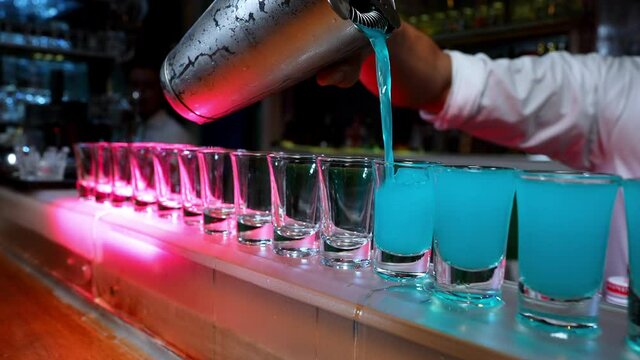 4K Professional male bartender pouring mixed blue liquor cocktail drink from cocktail shaker into shot glass on bar counter at nightclub. Mixologist barman making alcoholic drink serving to customer