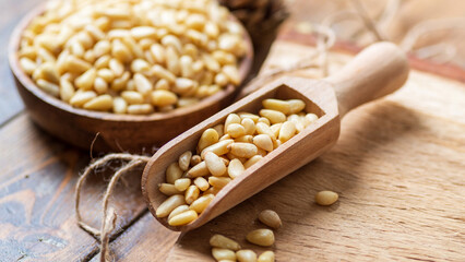 Round bowl with peeled pine nuts, scoop with nuts on the background of a round wooden board.