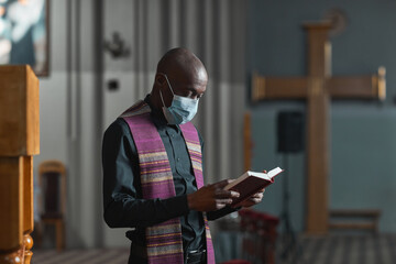 African priest in mask reading the Bible and holding the ceremony in the church
