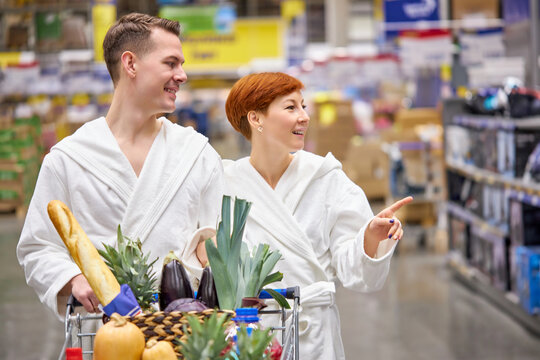 Couple In Bathrobes Choosing Goods In Grocery Store, Walking In Aisle