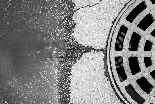 Old asphalt with a manhole cover on the road. After the rain. City environment. Top view close up.