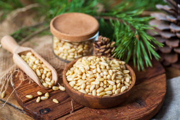 Pine nuts in a bowl, pine cone, branch, glass jar on a cutting board. Still life from natural ingredients, side view.