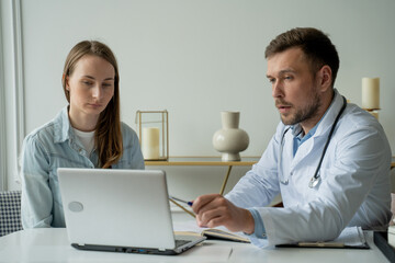 Obraz premium Therapist doctor man talking to patient. Adult male in white coat talks to female patient in medical office