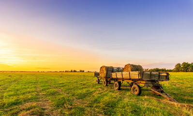 Old vintage carriage with hay stacks in green shiny field with beautiful sunset , hay cart in country valley during sunrise , wagon with haystacks and scenic view