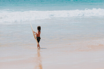 The small kid with a surfboard going into the ocean on an ocean beach.
