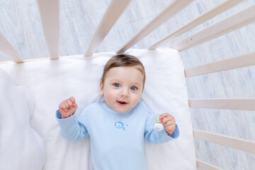 happy smiling baby boy in crib in blue bodysuit, cute joyful little baby in bedroom
