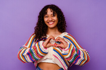 Young mixed race woman isolated on purple background smiling and showing a heart shape with hands.