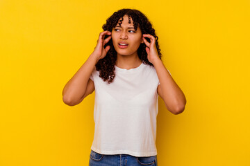 Young mixed race woman isolated on yellow background covering ears with fingers, stressed and desperate by a loudly ambient.
