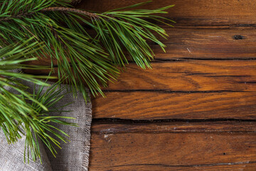 Gray linen fabric lies in folds on a dark wooden table, next to a pine branch with green needles. 