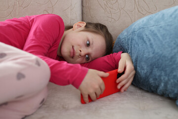 Little girl lies on couch and looks at smartphone screen