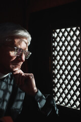 Senior man in eyeglasses sitting behind the grid and listening to faithful person
