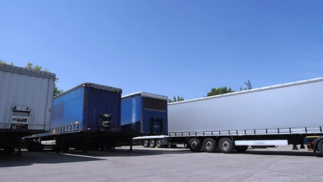 White lorry with cargo trailer drives back into parking place and parks with other cargo trailers.