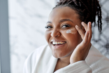 Afro-american Female Doing Skincare Procedure In After Shower, Using Cosmetics, Apply Anti-wrinkle Cream On Face