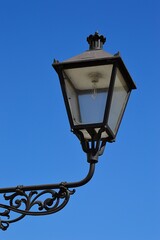 Fototapeta na wymiar Decorative vintage street light in style of 19th century gas street lantern sunbathing in spring daylight sunshine, clear blue skies in background.