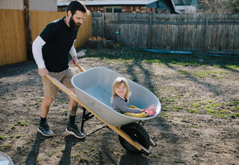Father pushing daughter in a wheelbarrow around the back yard - Powered by Adobe