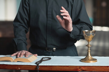 Close-up of priest standing at the altar with Bible and rosary beads