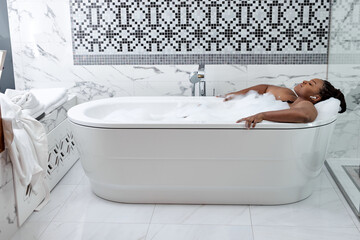 African woman in bath. Bathtub with bubbles and foam. Skincare therapy and treatment in hot tub in spa