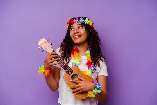 Fototapeta Young hawaiian woman playing ukelele isolated on purple background