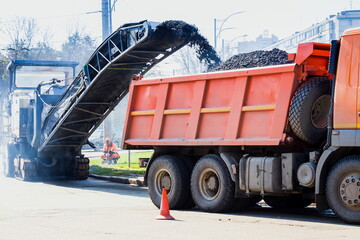 Road construction working. The road milling machine removes old asphalt and loads milled asphalt into the dump truck. Road repair process © decorator