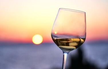 Close up image of glass of wine in woman's hand with the sea and sunset in the background. Summer holiday, vacation concept.