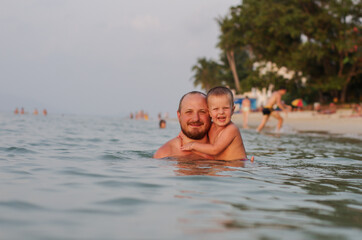 dad and son swim in the sea at sunset. they smile at the camera. the baby and his father spend a happy time on the beach