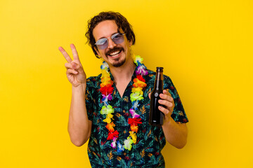 Young caucasian man wearing a hawaiian necklace holding a beer isolated on yellow background joyful...