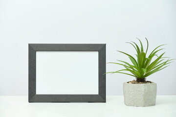 Gray wooden frame mockup with a plant in a concrete flowerpot on a white marble table.