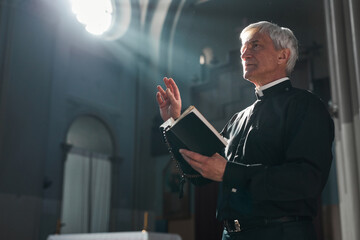 Senior priest standing with the Bible during ceremony in the church