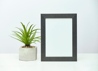 Gray wooden vertical frame mockup with a plant in a concrete flowerpot on a white marble table.