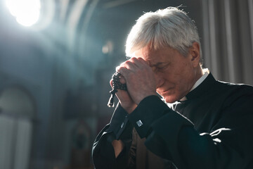 Senior priest holding rosary beads praying while sitting in the church