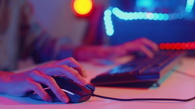 Close-up hands shot asia girl gamer use keyboard and mouse controller play video game with neon light computer in desk at home. Online esport streaming game online, Home quarantine activity concept.
