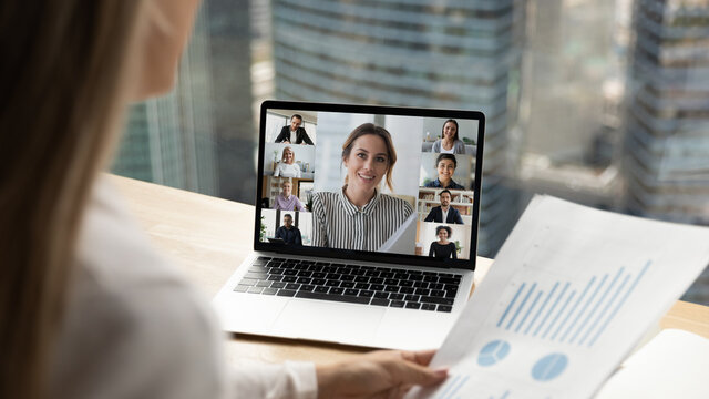 Back view of woman talk on video call with multiethnic colleagues discuss business paperwork online together. Diverse employees have webcam digital zoom meeting on laptop. Virtual event concept.