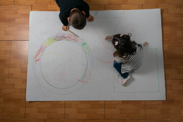 vista superior de un niño y niña dibujando y pintando una pancarta gigante figuras geométricas en el suelo .