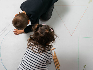 vista superior de un niño y niña dibujando y pintando una pancarta gigante figuras geométricas...