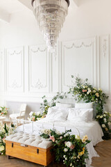 a white bed by a large window. the white bed is decorated with flowers. decorated in floral decor. bedroom with large bed