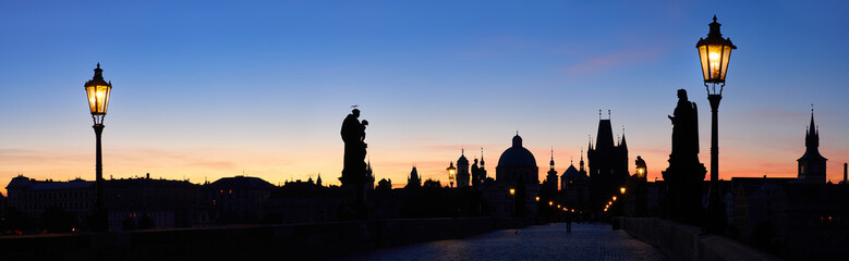 Prague banner, Charles Bridge at night. Silhouettes of statues, Old Bridge Tower, churches and spires of Old Prague against blue and pink sky. panoramic image.