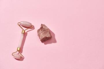 Rose quartz facial massage roller and natural raw rough stone isolated over pink background