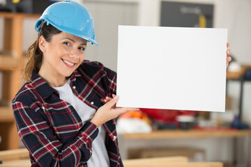 smiling female worker wearing a safety helmet holding blank banner