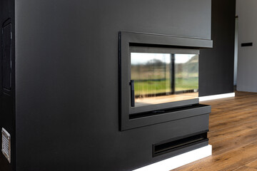 A modern fireplace with a closed combustion chamber standing in the living room, painted black,...