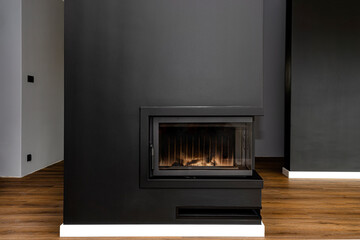 A modern fireplace with a closed combustion chamber standing in the living room, painted black, with a washed corner pane.