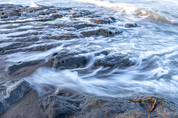 Winter sea at dawn. Backwash on a beach with outcropping rocks. Elegant silky effect for moving water in the foreground.