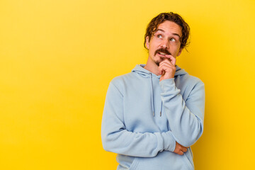 Young caucasian man isolated on yellow background relaxed thinking about something looking at a copy space.