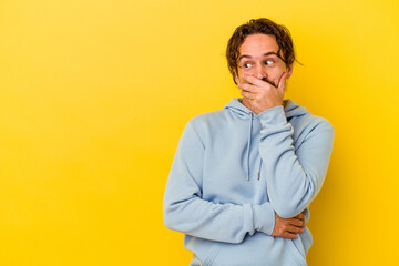 Young caucasian man isolated on yellow background thoughtful looking to a copy space covering mouth with hand.