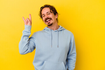 Young caucasian man isolated on yellow background showing a horns gesture as a revolution concept.