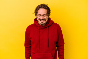 Young caucasian man isolated on yellow background laughs and closes eyes, feels relaxed and happy.