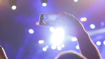 Close up: man hands taking photo or recording video of live music concert with smartphone at nightclub - close up. Bright colorful stage lighting with lens flares. Photography, technology concept