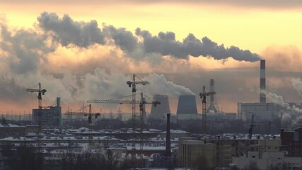 Construction cranes. Smoke from pipes of a thermal power plant in the background. Sunset. Winter. .