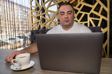 a man sitting with a laptop in a cafe chatting online while drinking tea