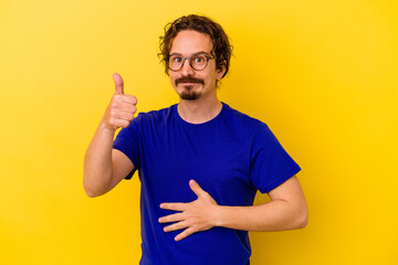 Young caucasian man isolated on yellow background touches tummy, smiles gently, eating and satisfaction concept.