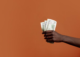 Black female hand hold dollars on orange background